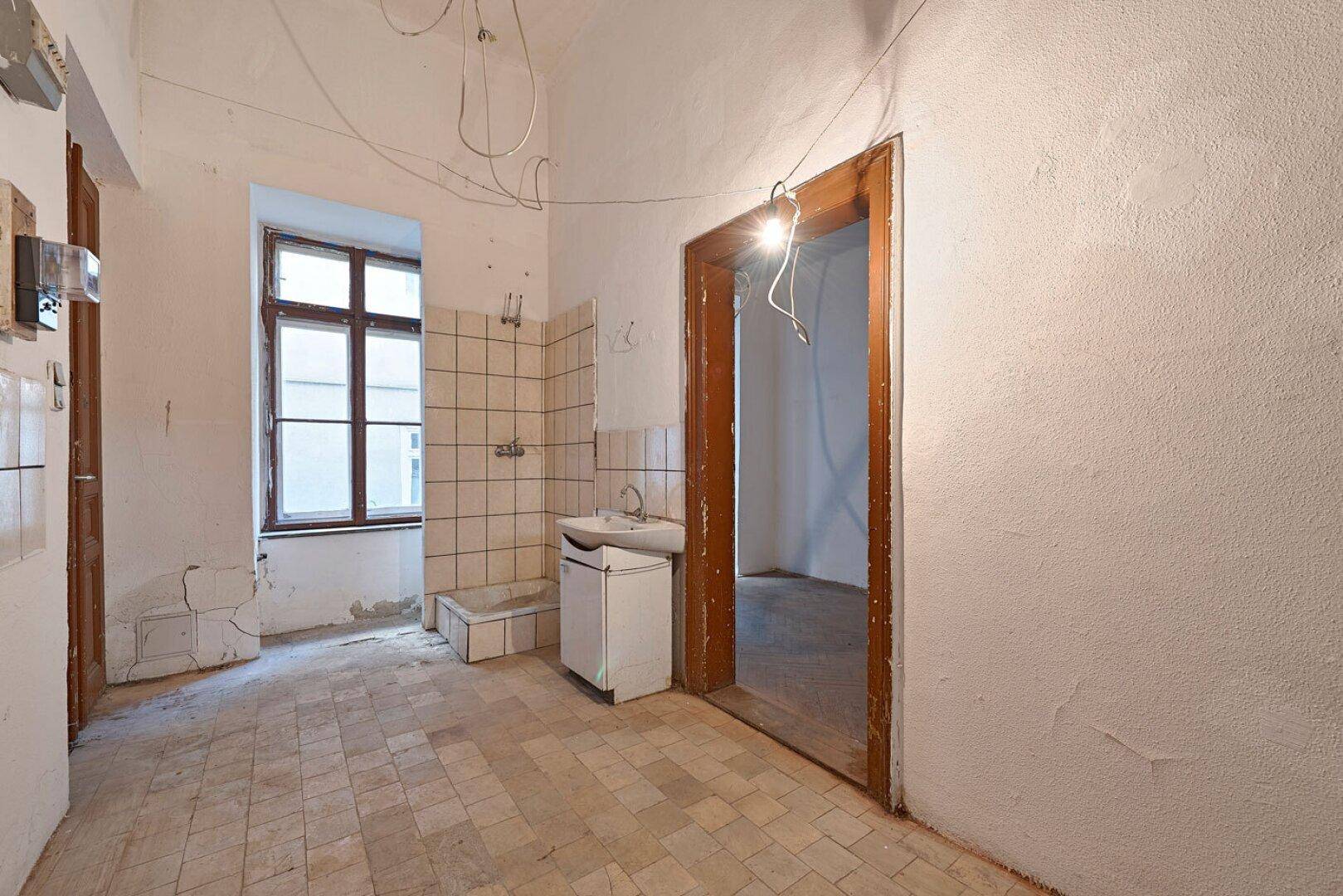 Unrenovierte Küche mit Fliesenboden, einem Waschbecken und einem Fenster, das auf den Innenhof blickt.
