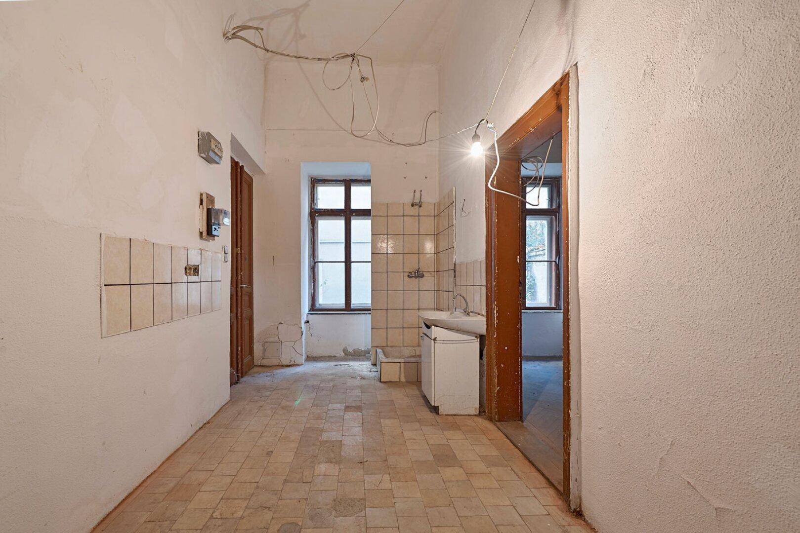 Unrenovierter Küchenbereich mit Fliesenboden, einem Fenster und sichtbaren Wandfliesen.