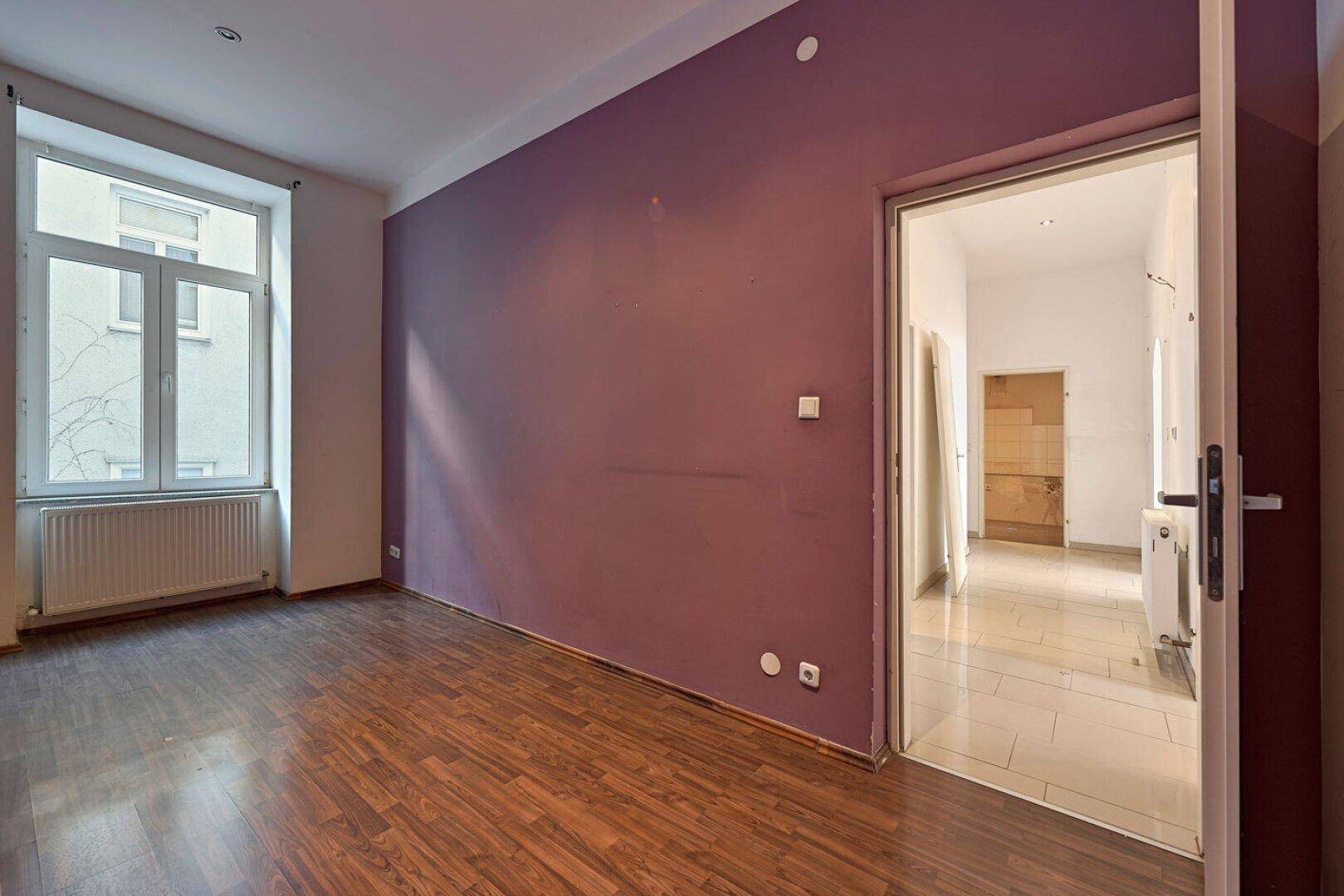 Geräumiges Zimmer mit lila Wand, Holzboden und Blick auf die Straße.
