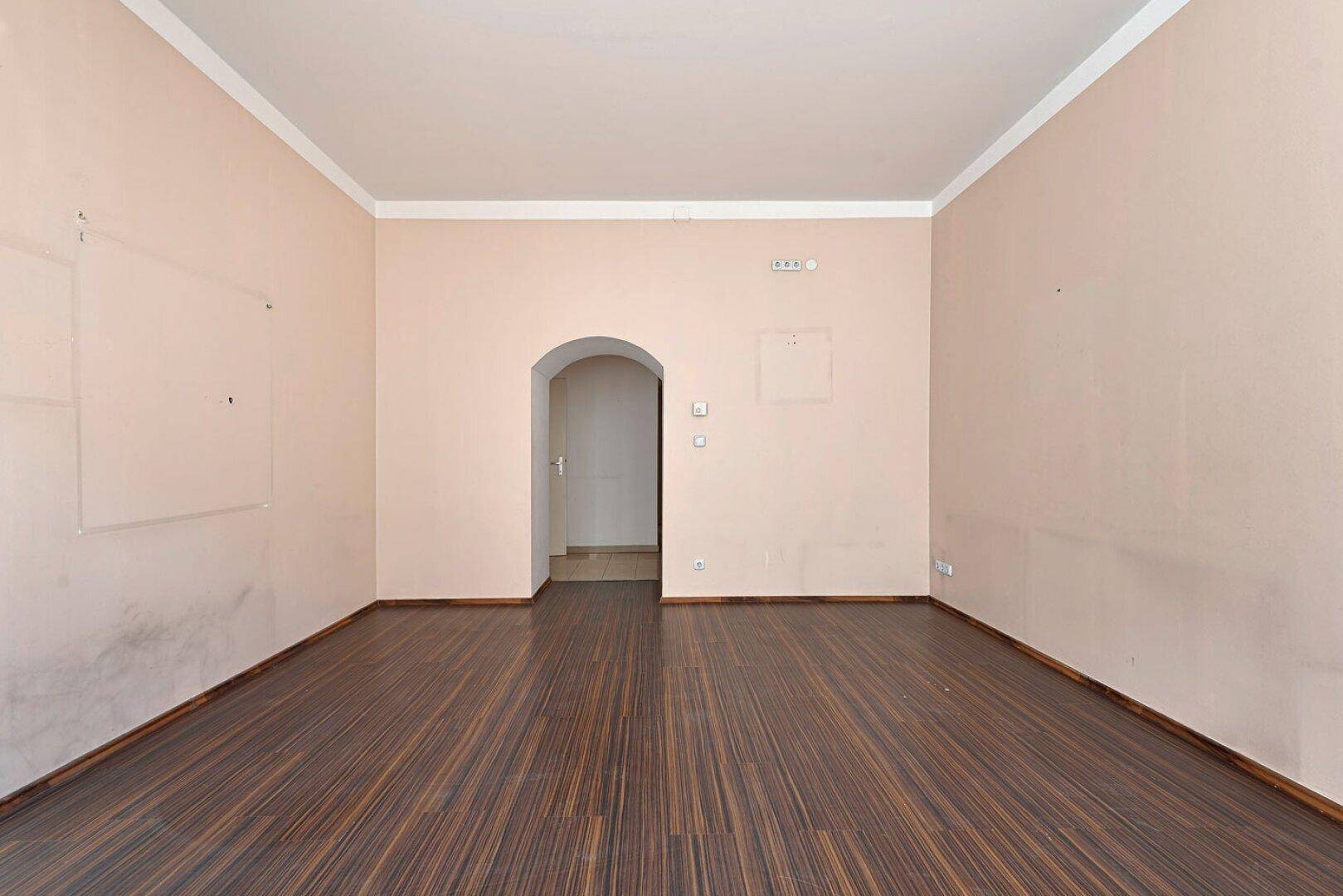 Leeres Zimmer mit Holzboden und einem Rundbogen, der zu einem Flur führt.