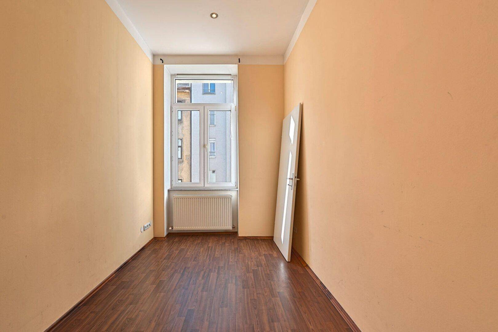 Helles Zimmer mit orangefarbenen Wänden, Holzboden und einem Fenster.