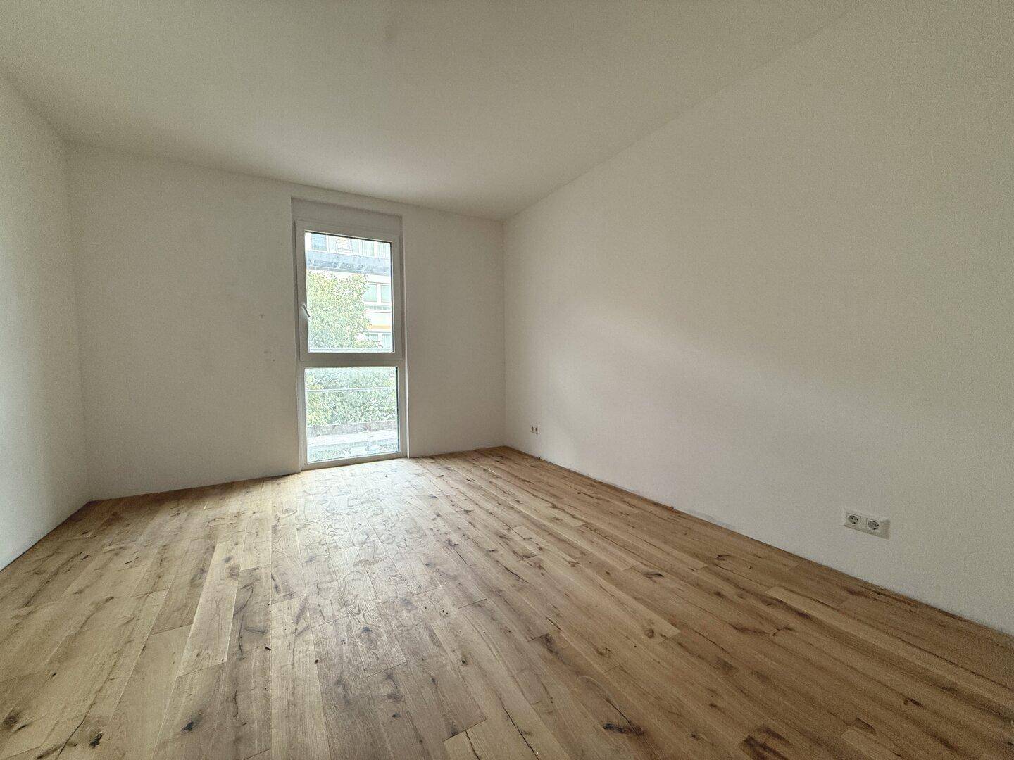 Helles Zimmer mit neuem Holzplankenboden und großem Fenster, ideal als Schlaf- oder Arbeitszimmer.