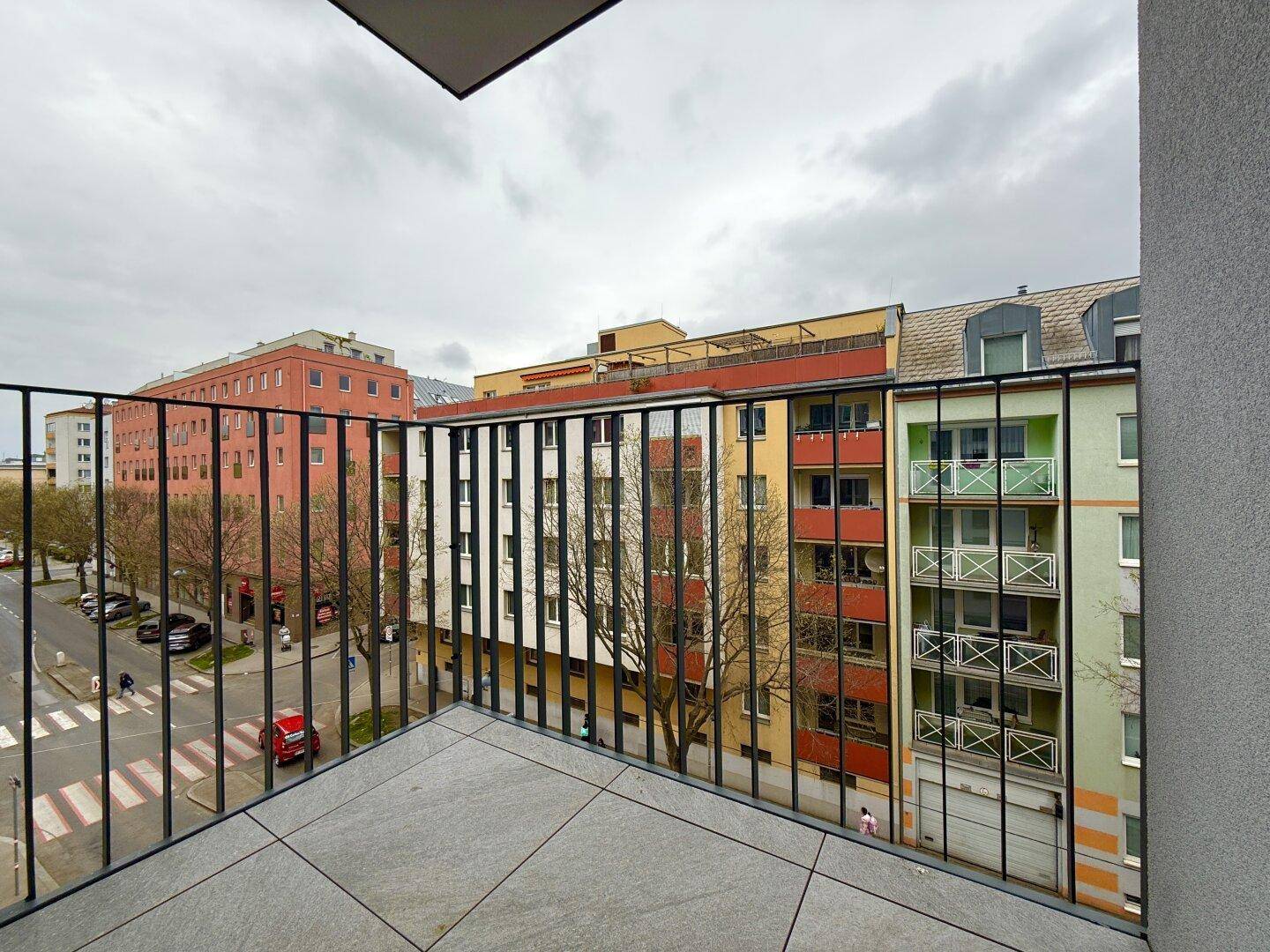 Balkon mit Fliesenboden und Blick auf die umliegenden Gebäude und die Straße.