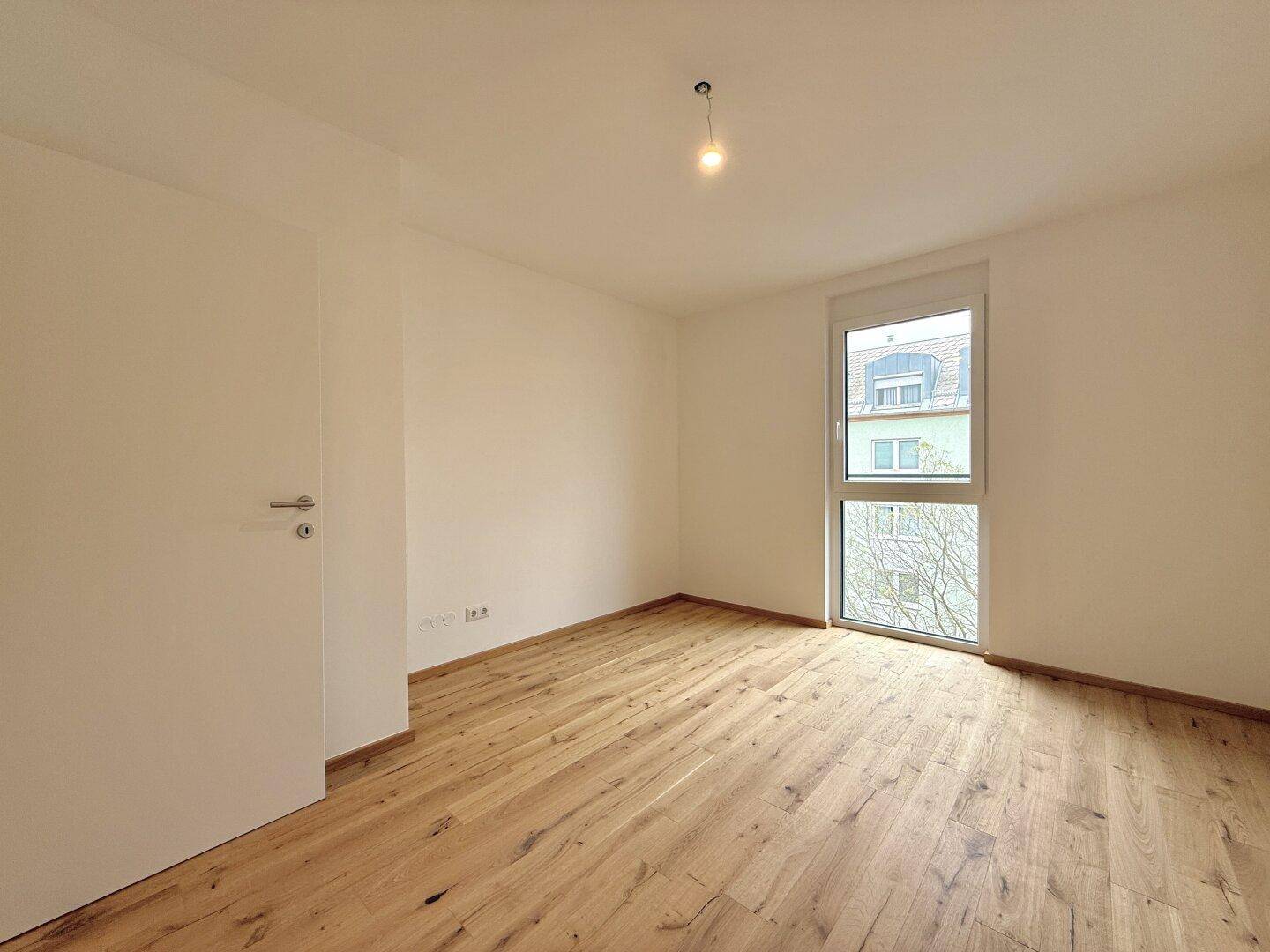 Gemütliches Schlafzimmer mit hellem Holzparkett und großem Fenster für viel Tageslicht.