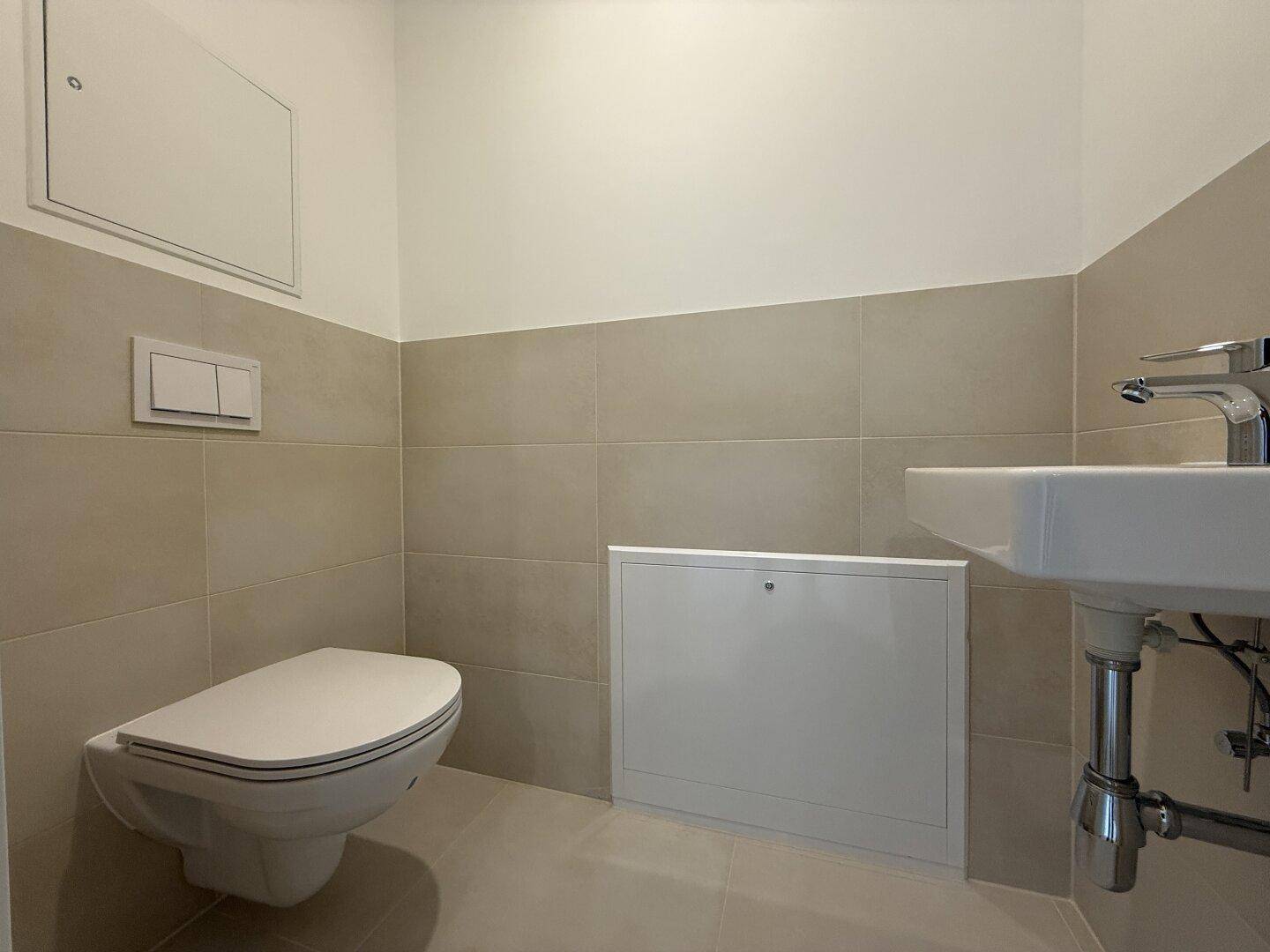 Modernes Gäste-WC mit wandhängendem WC, Waschbecken und hellen Wandfliesen.