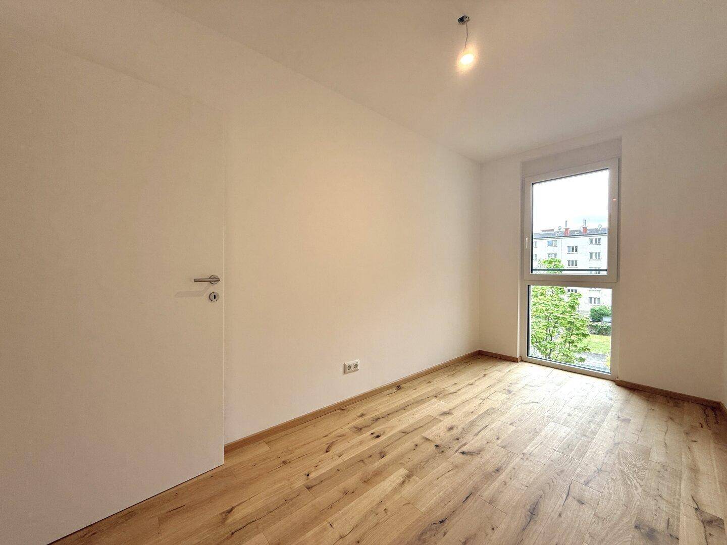 Helles Zimmer mit Holzboden und großem Fenster, ideal als Schlaf- oder Arbeitszimmer.