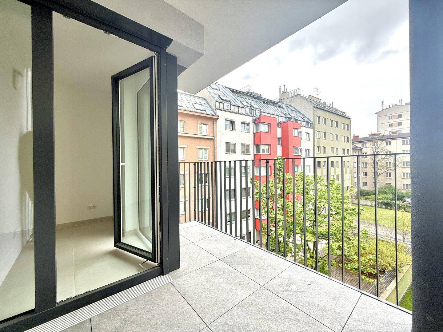 Geräumiger Balkon mit Fliesenboden und Blick auf die umliegenden Gebäude.