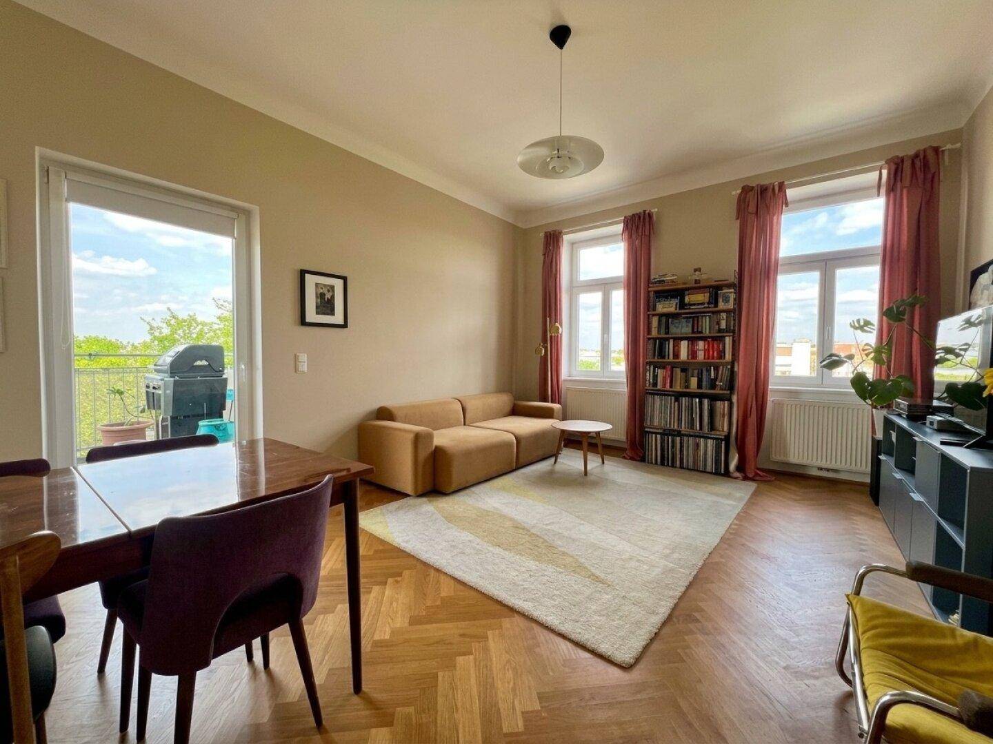 Heller Wohn- und Essbereich mit Fischgrätparkett, beigen Wänden und Zugang zum Balkon.
