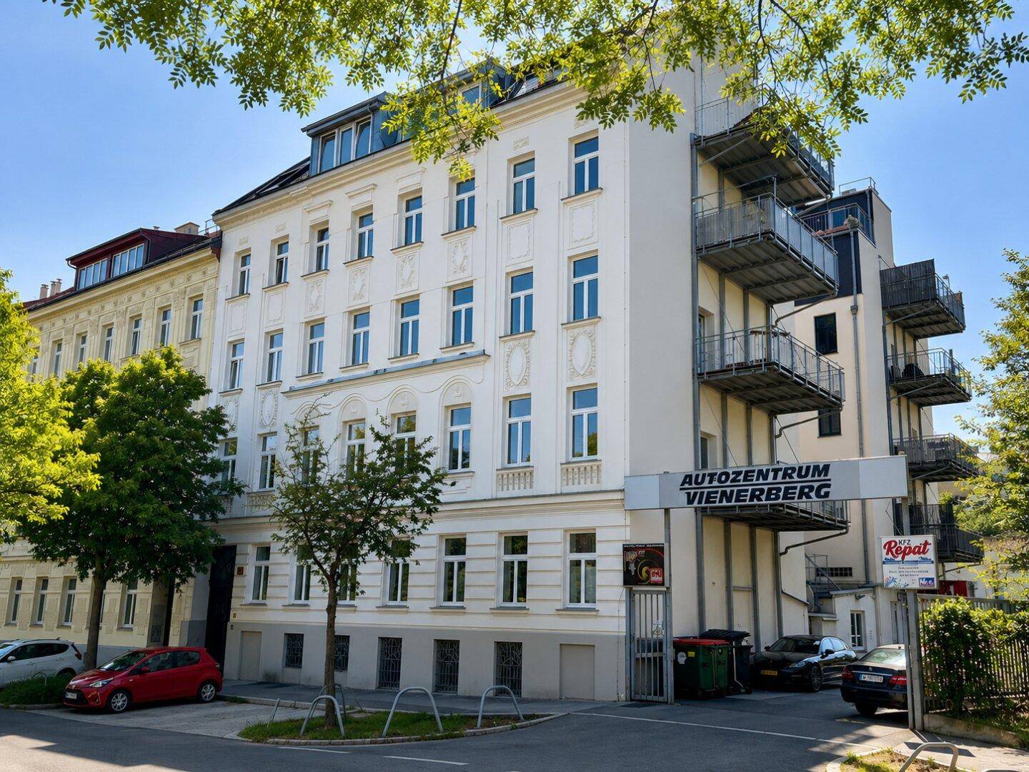 Außenansicht eines Mehrfamilienhauses mit Balkonen und umliegenden Bäumen an einem sonnigen Tag.
