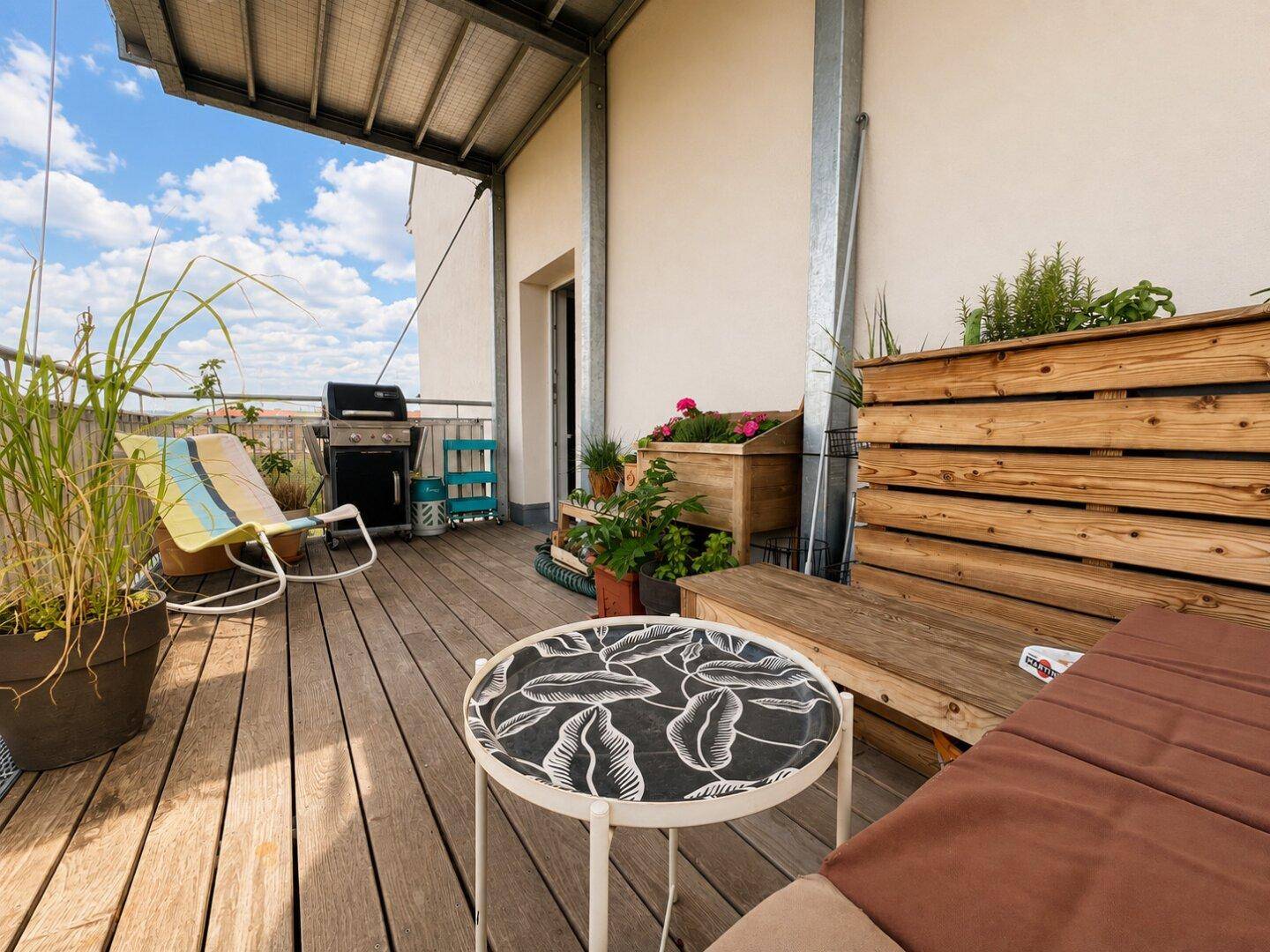 Geräumiger Balkon mit Holzboden, Grill und Sitzgelegenheiten unter blauem Himmel.