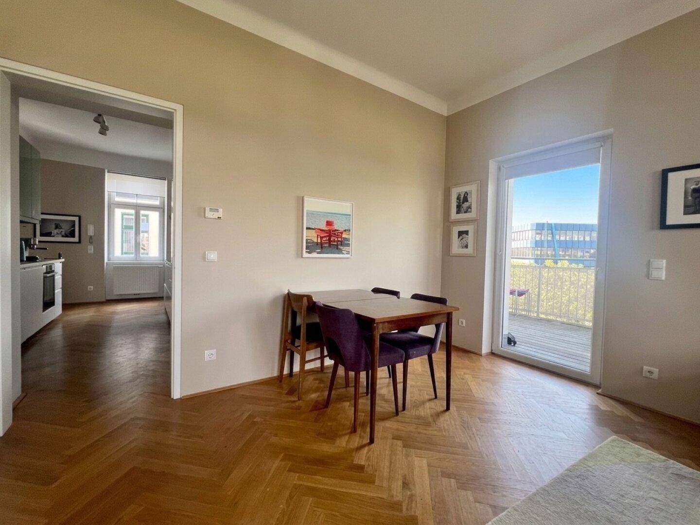 Heller Essbereich mit Holztisch, Fischgrätparkett und Zugang zum Balkon.