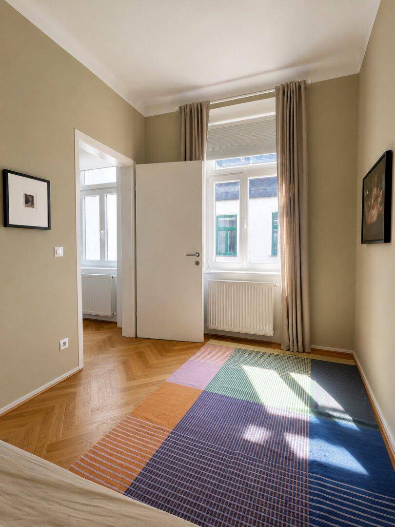 Schlafzimmer mit Fischgrätparkett, beigen Wänden und Blick auf den Innenhof.