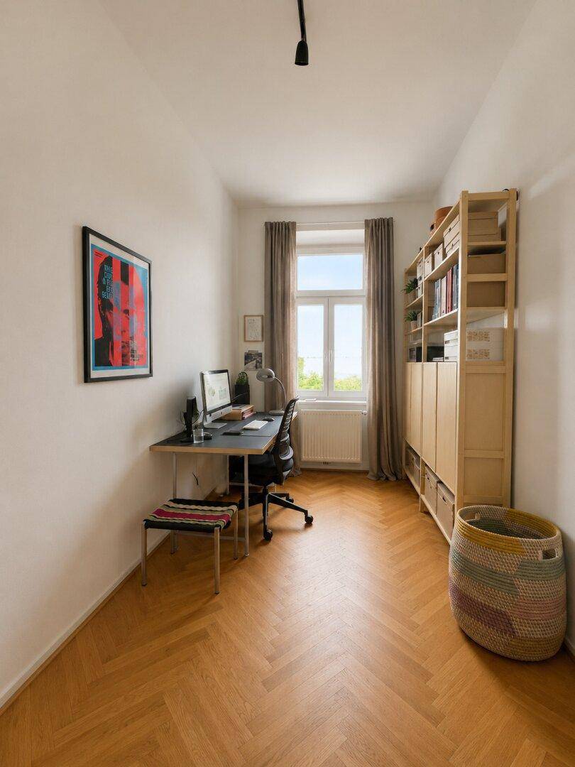Helles Arbeitszimmer mit Fischgrätparkett, Schreibtisch und Bücherregal.