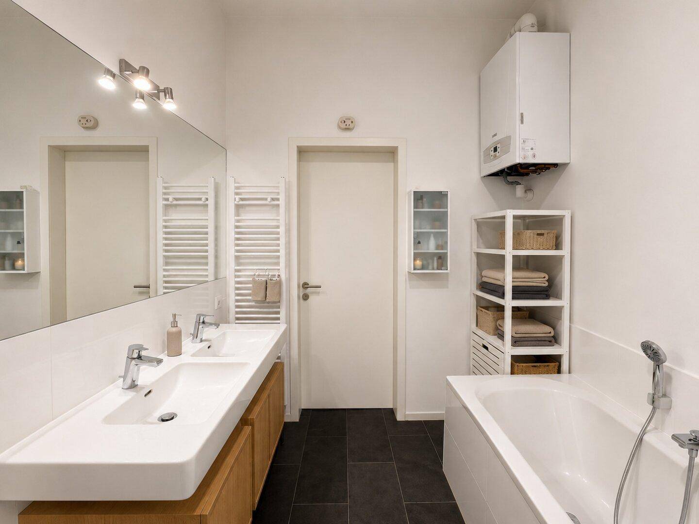 Helles Badezimmer mit Doppelwaschbecken, Badewanne und Heizkörper.