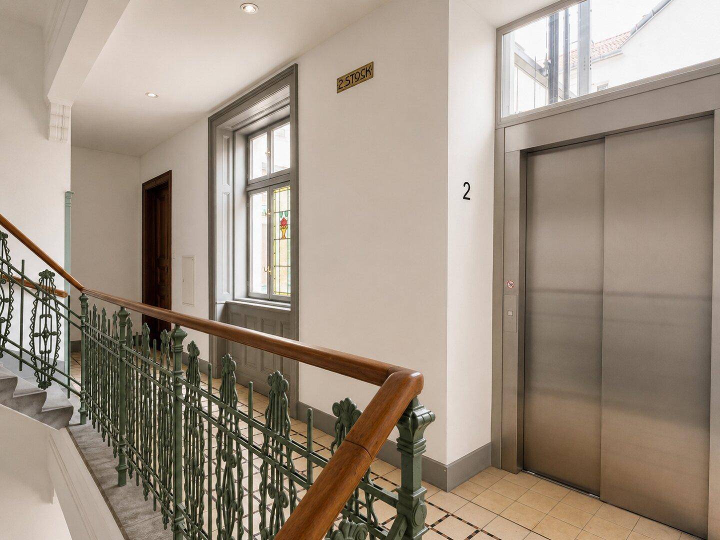 Heller Flur mit Aufzug, Treppenhaus und traditionellem Fliesenboden.