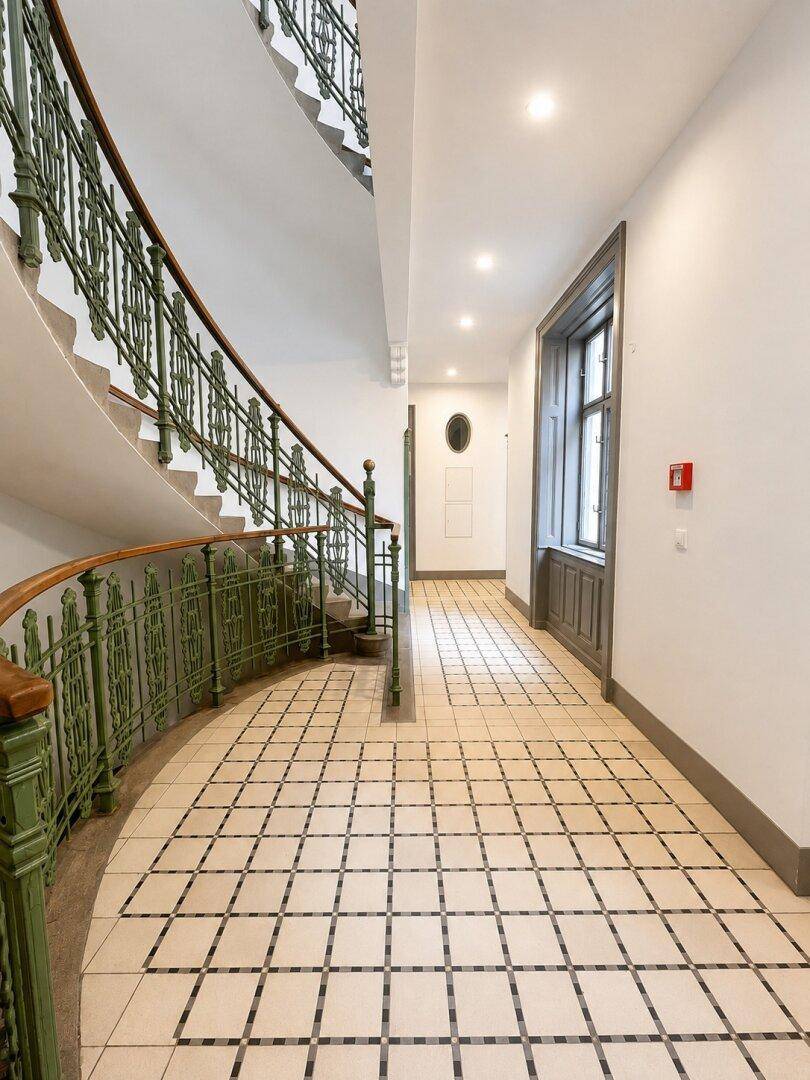 Elegantes Treppenhaus mit schmiedeeisernem Geländer und gemustertem Fliesenboden.