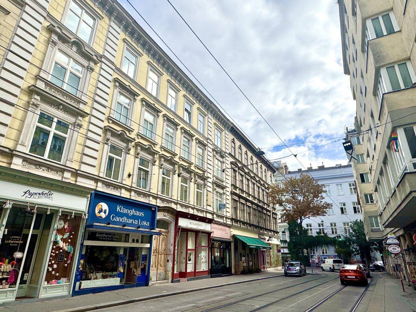 Seitenansicht eines historischen Gebäudes an einer belebten Stadtstraße mit Geschäften und Verkehr.