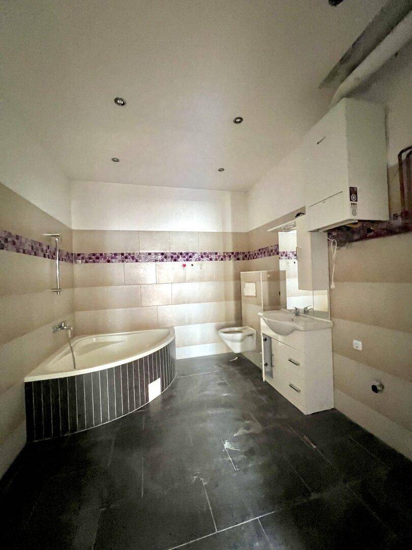 Modernes Badezimmer mit Eckbadewanne, Waschtisch und dunklen Fliesen, gut beleuchtet.