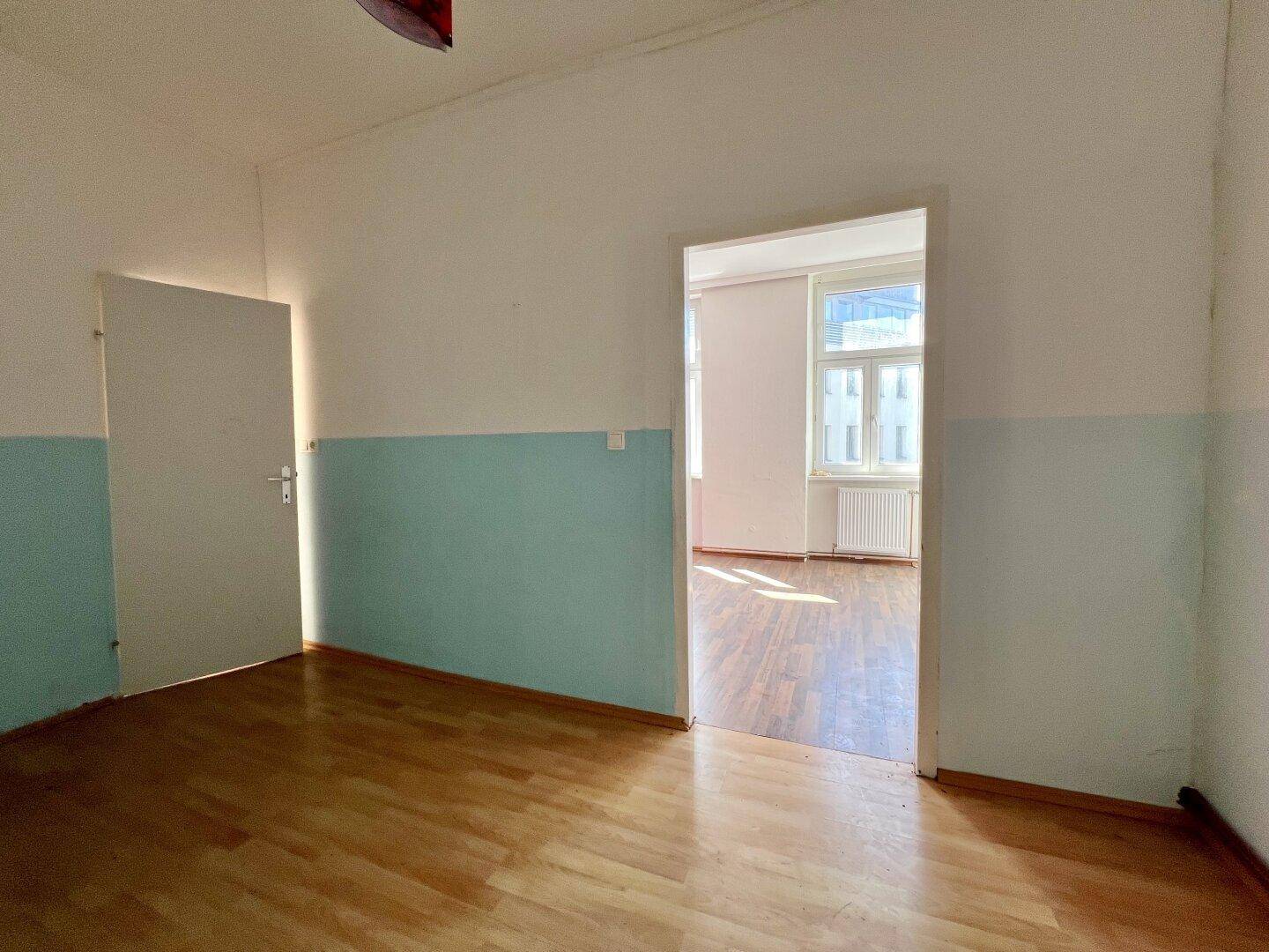 Zwei leere Zimmer mit Holzboden und hellblauen Wänden, verbunden durch einen offenen Durchgang.