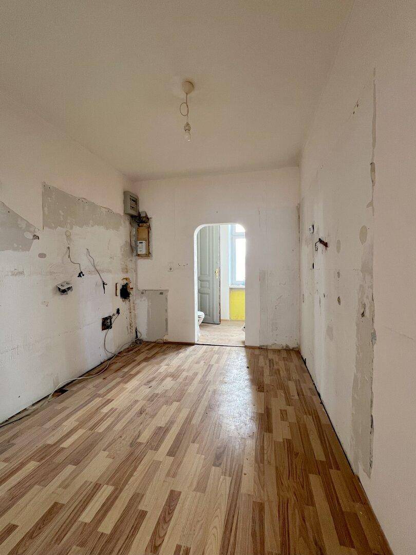 Leere Küche in Renovierung mit Holzboden und vorbereiteten Anschlüssen für Geräte.