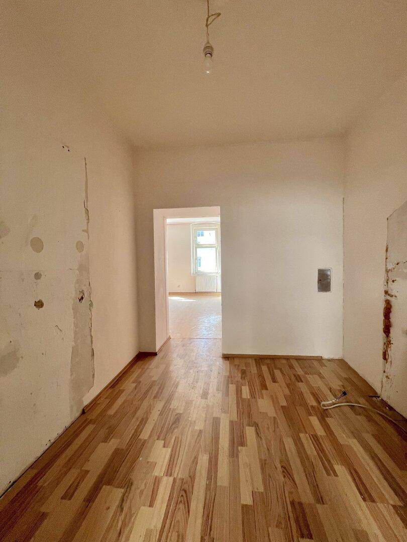 Langer Flur mit Holzboden und teilweise renovierten Wänden, führt zu einem weiteren Raum.