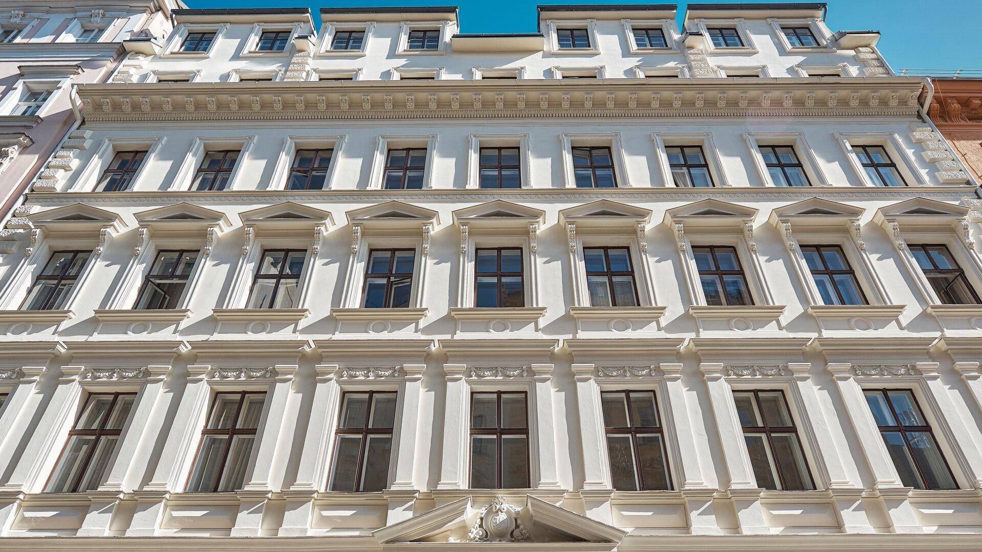 Eindrucksvolle weiße Fassade eines Altbaus mit vielen Fenstern und dekorativen Elementen.