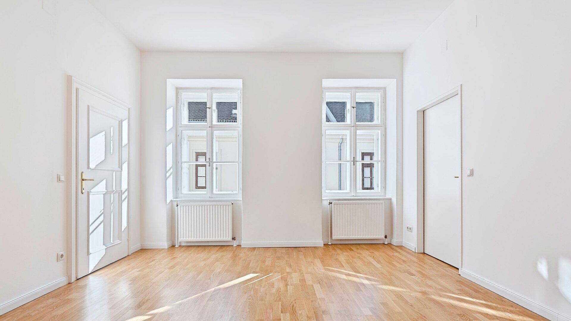 Lichtdurchflutetes Zimmer mit hellem Holzplankenboden und großen Fenstern, bereit zur individuellen Gestaltung.