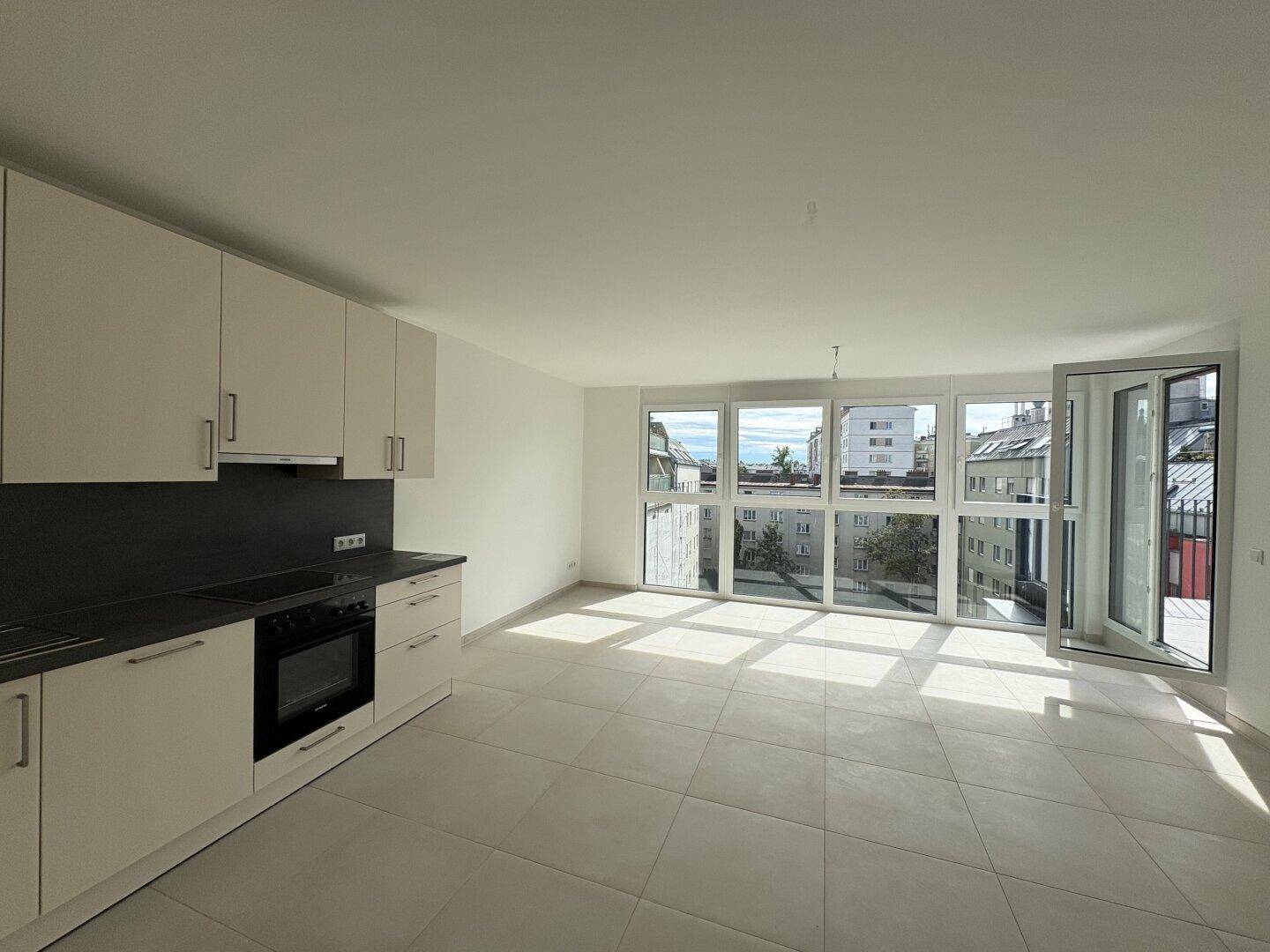 Lichtdurchfluteter Wohn-Essbereich mit moderner Küchenzeile, Fliesenboden und Zugang zum Balkon.