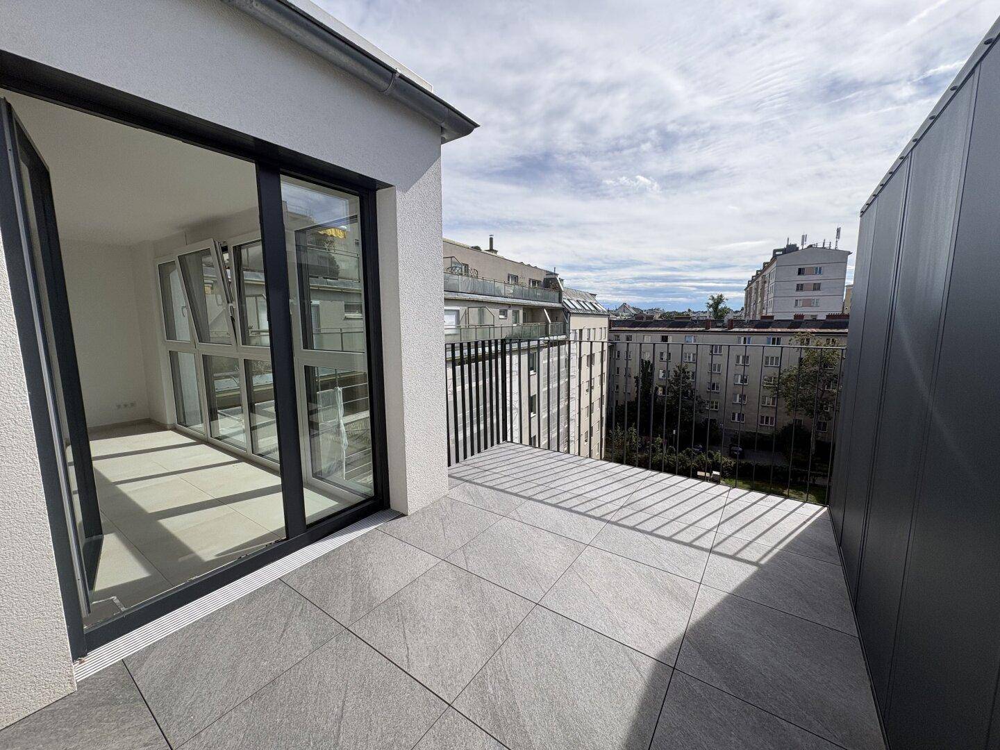 Moderner Balkon mit Fliesenboden und Blick auf die umliegende Stadtlandschaft.