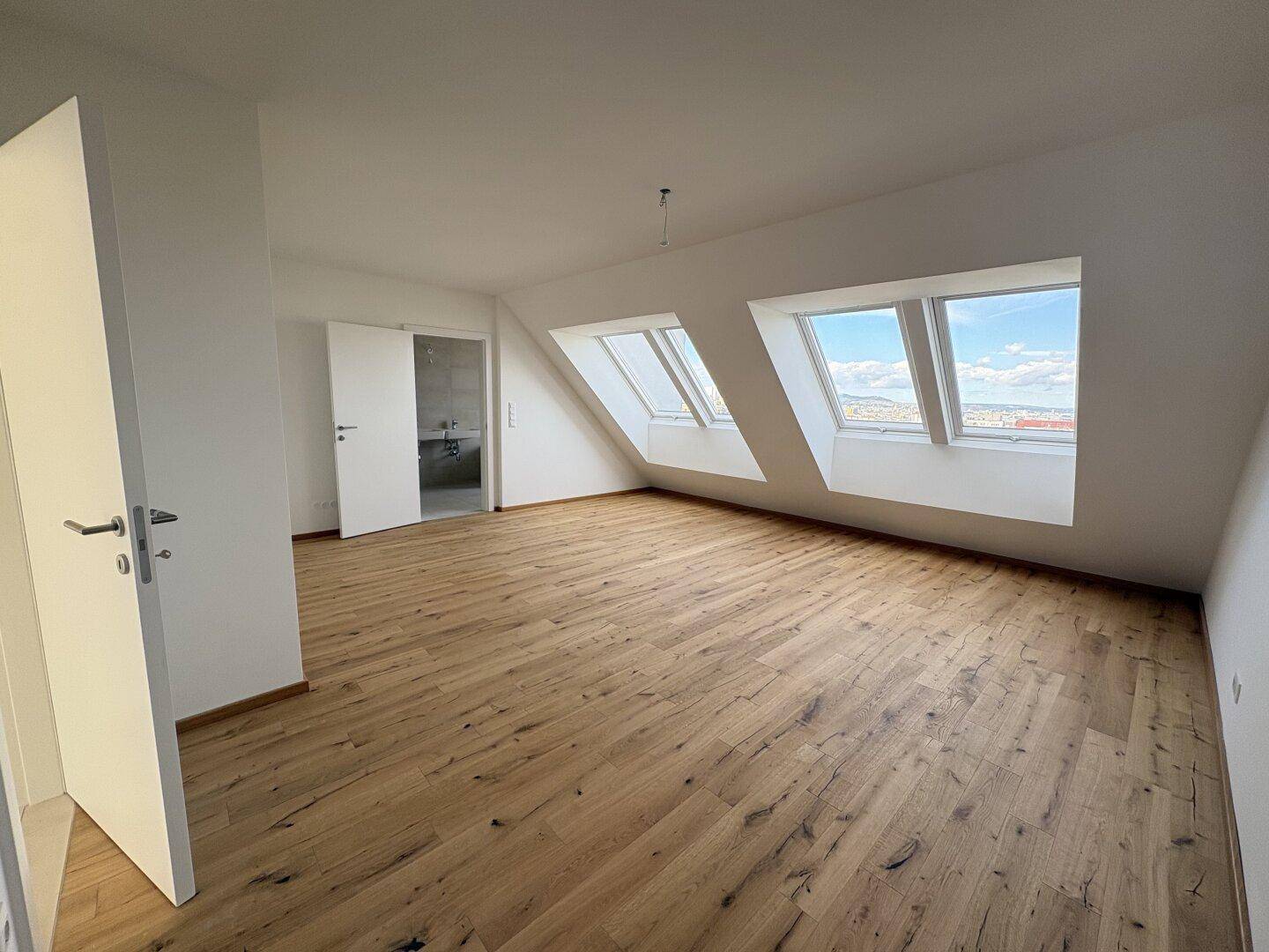 Geräumiges Schlafzimmer mit Holzboden, schrägen Wänden und Dachfenstern für viel Tageslicht.