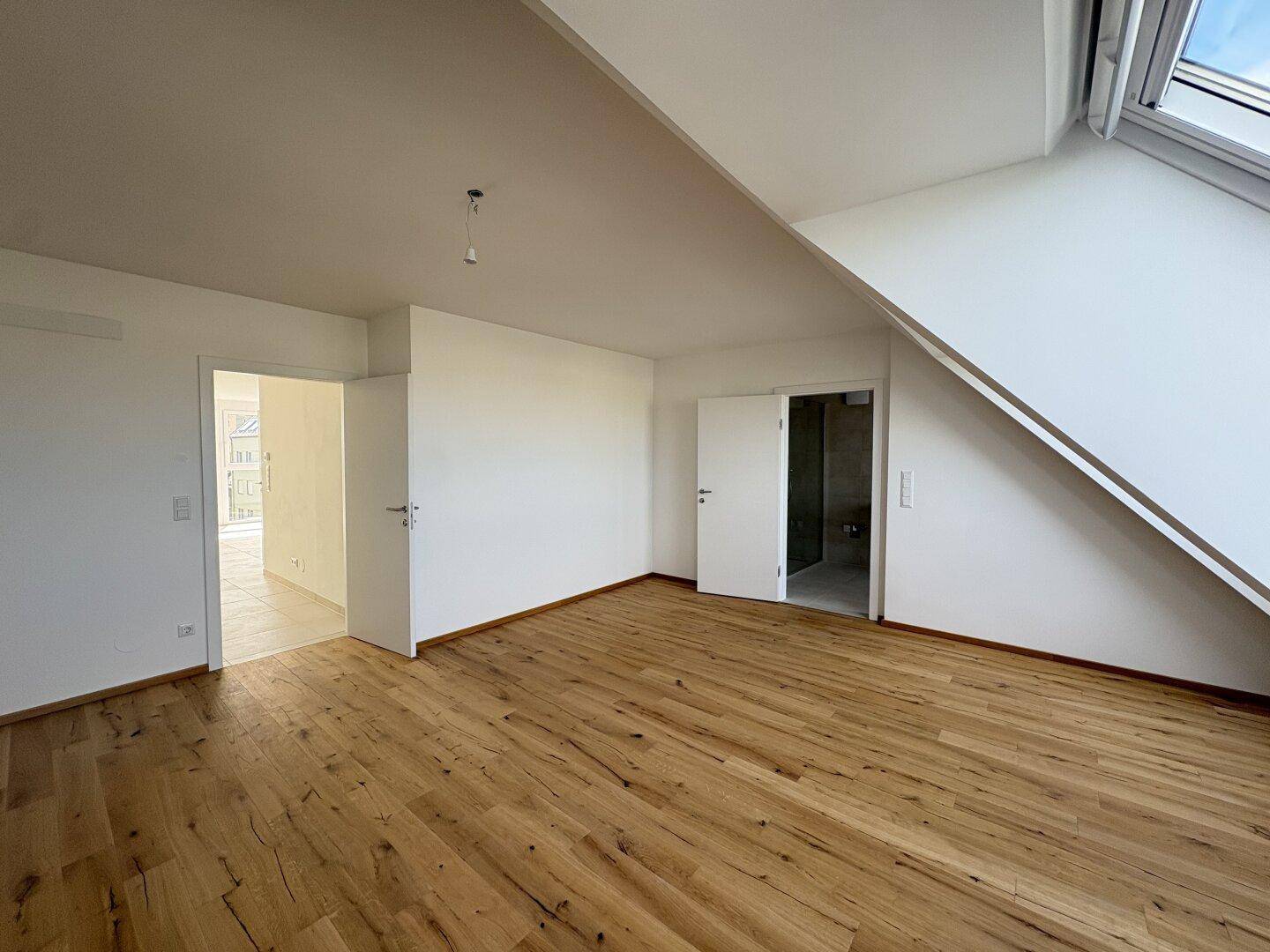 Schlafzimmer im Dachgeschoss mit Holzboden, schrägen Wänden und Zugang zu weiteren Räumen.