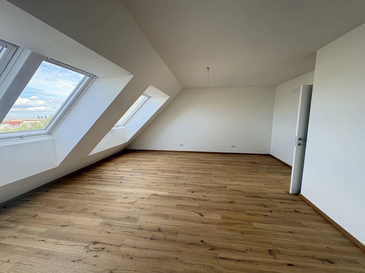 Helles Schlafzimmer mit Holzboden und großen Dachfenstern, die einen weiten Blick ermöglichen.
