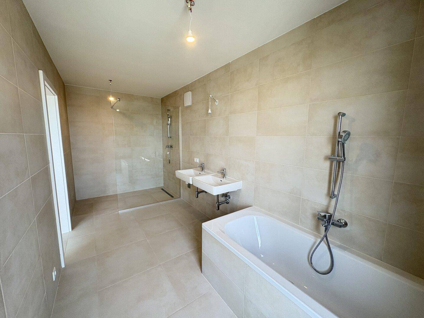 Helles Badezimmer mit Fliesen, begehbarer Dusche, Badewanne und modernen Armaturen.