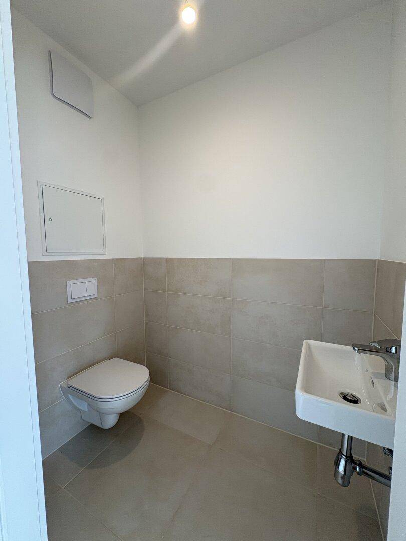 Separates Gäste-WC mit Wand-WC, kleinem Waschbecken und modernen Fliesen.