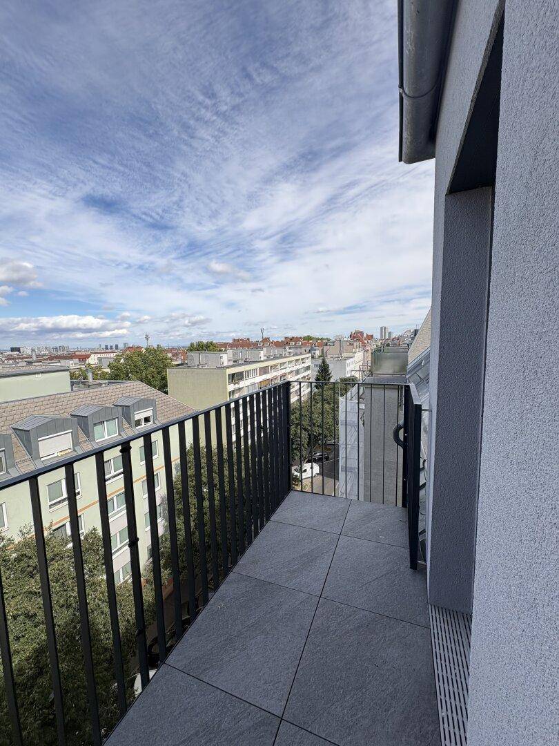Schmaler Balkon mit Fliesenboden und weitem Blick über die Dächer der Stadt.