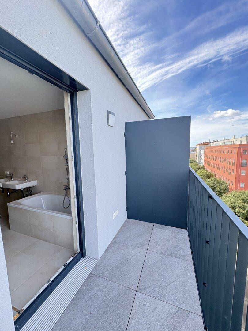 Balkon mit Fliesenboden und Zugang zu einem Badezimmer, bietet einen Blick auf die Umgebung.