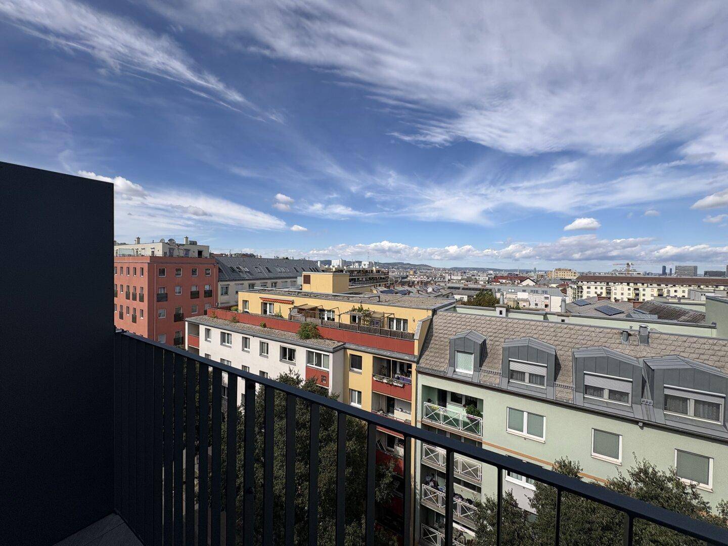 Ausblick vom Balkon auf die Stadt mit Gebäuden und Bäumen unter blauem Himmel.