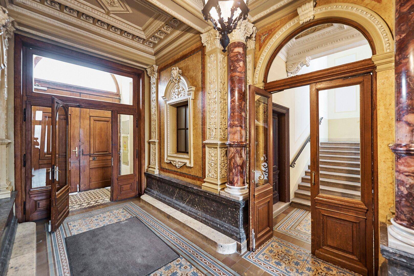 Prunkvoller Eingangsbereich mit Marmorsäulen, verzierten Decken und einer eleganten Treppe, die in die oberen Stockwerke führt.