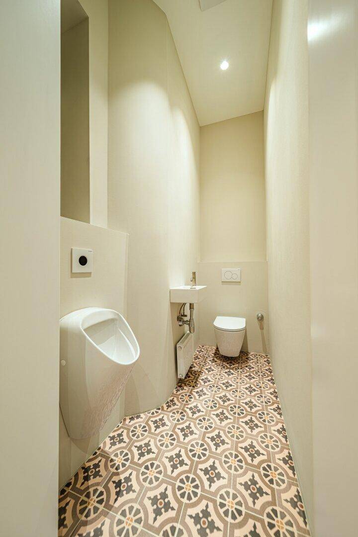 Modernes Gäste-WC mit Urinal, wandhängender Toilette und gemusterten Fliesen auf dem Boden.