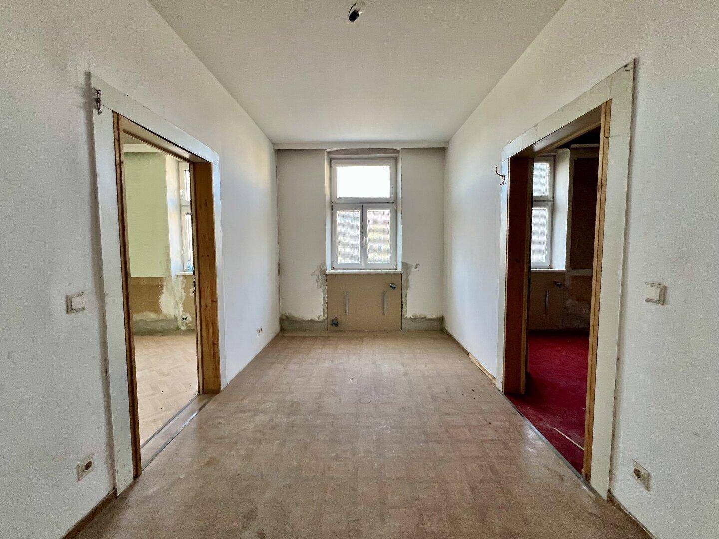 Langer Flur mit Parkettboden und Türen zu weiteren Räumen, bereit für die Renovierung.