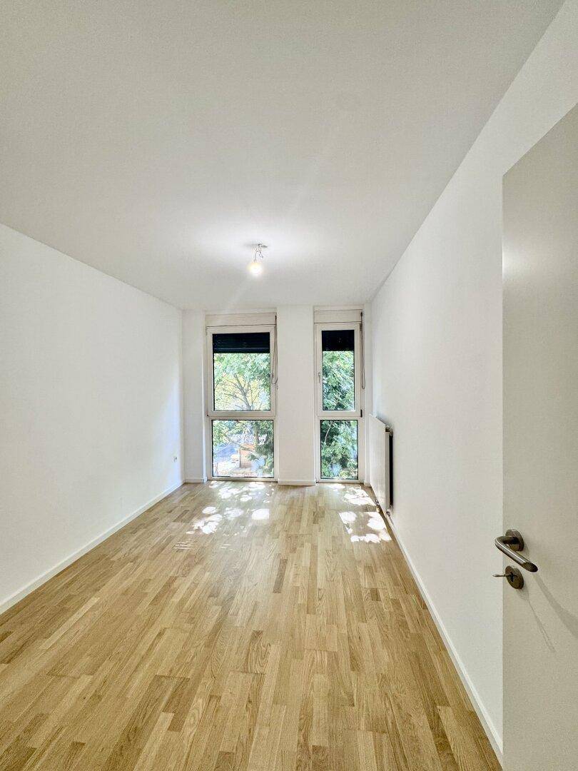 Helles Schlafzimmer mit Parkettboden und zwei Fenstern, die viel Licht hereinlassen.