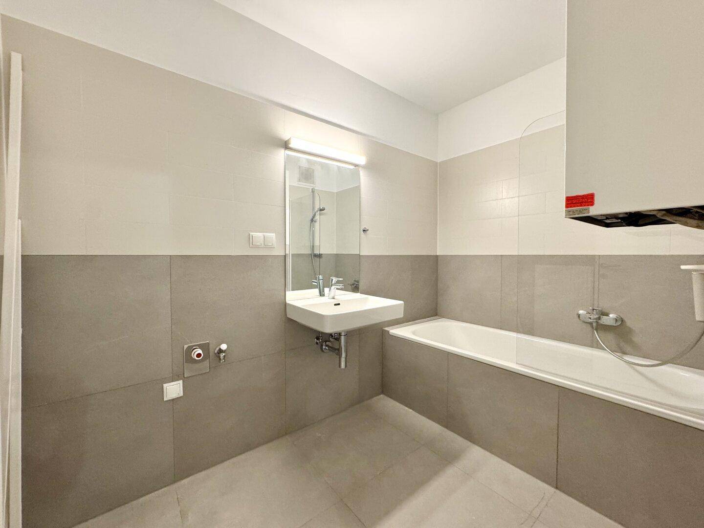 Modernes Badezimmer mit Badewanne, Waschbecken und grauen Fliesen an Wänden und Boden.