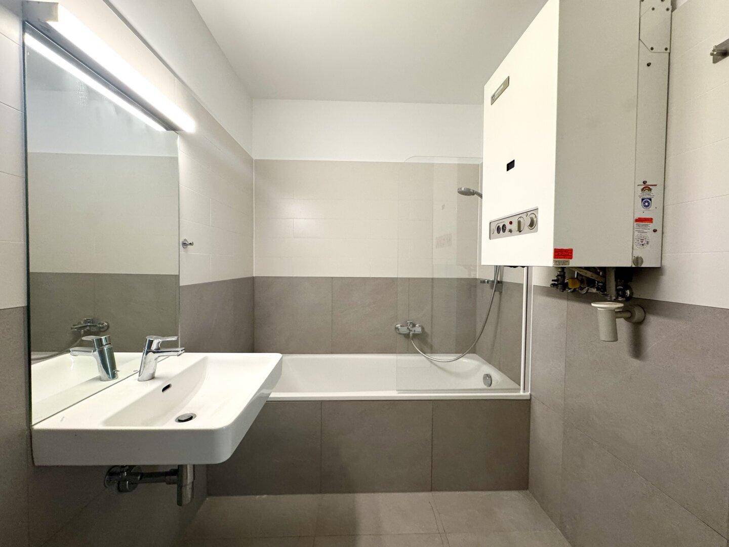 Funktionales Badezimmer mit Badewanne, Duschvorrichtung und wandmontiertem Waschbecken.