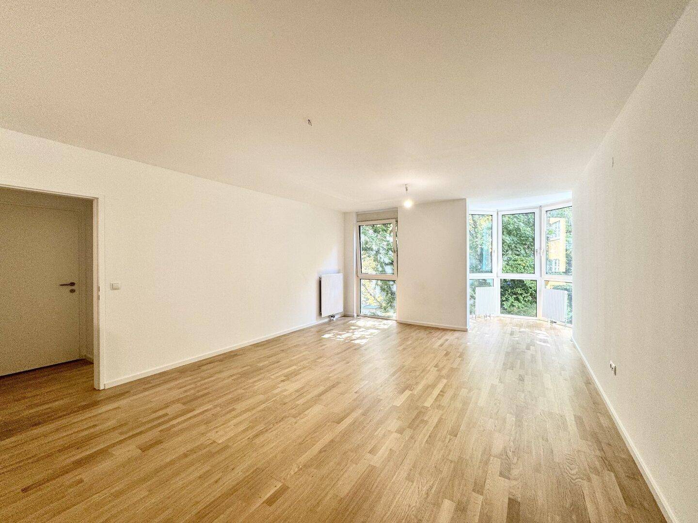 Geräumiges Wohnzimmer mit hellem Parkettboden und großen Fenstern für viel Tageslicht.