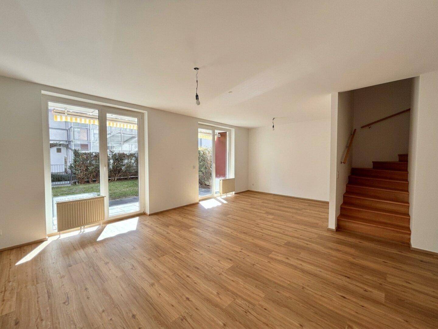 Geräumiges, leeres Wohn-Esszimmer mit Holzboden und Treppe, bietet Zugang zum Außenbereich.