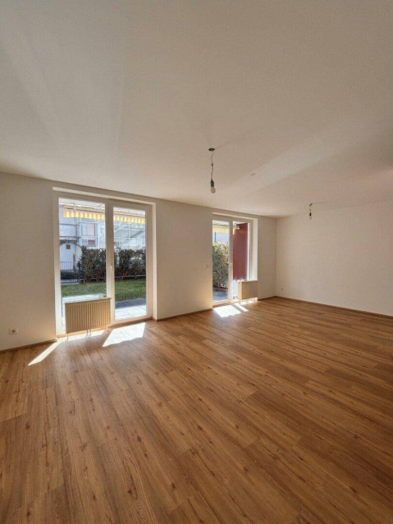 Lichtdurchfluteter, leerer Wohnbereich mit Holzboden und großen Fenstern zum Garten.