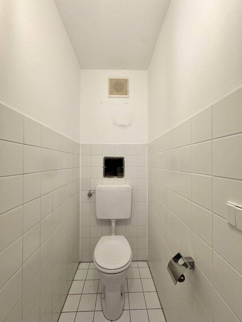 Separates WC mit Wandfliesen, Toilette und Lüftungsgitter, funktional und sauber.