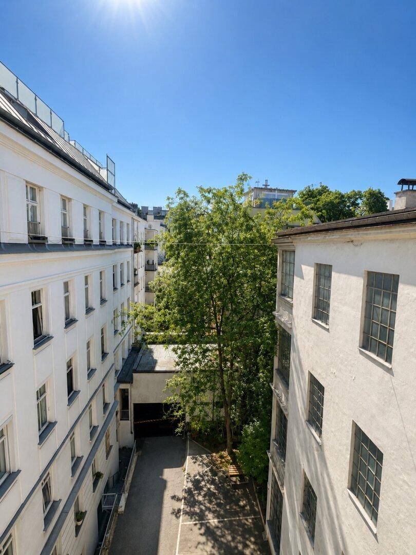 Sonniger Blick auf einen grünen Innenhof, umgeben von weißen Gebäuden mit vielen Fenstern.