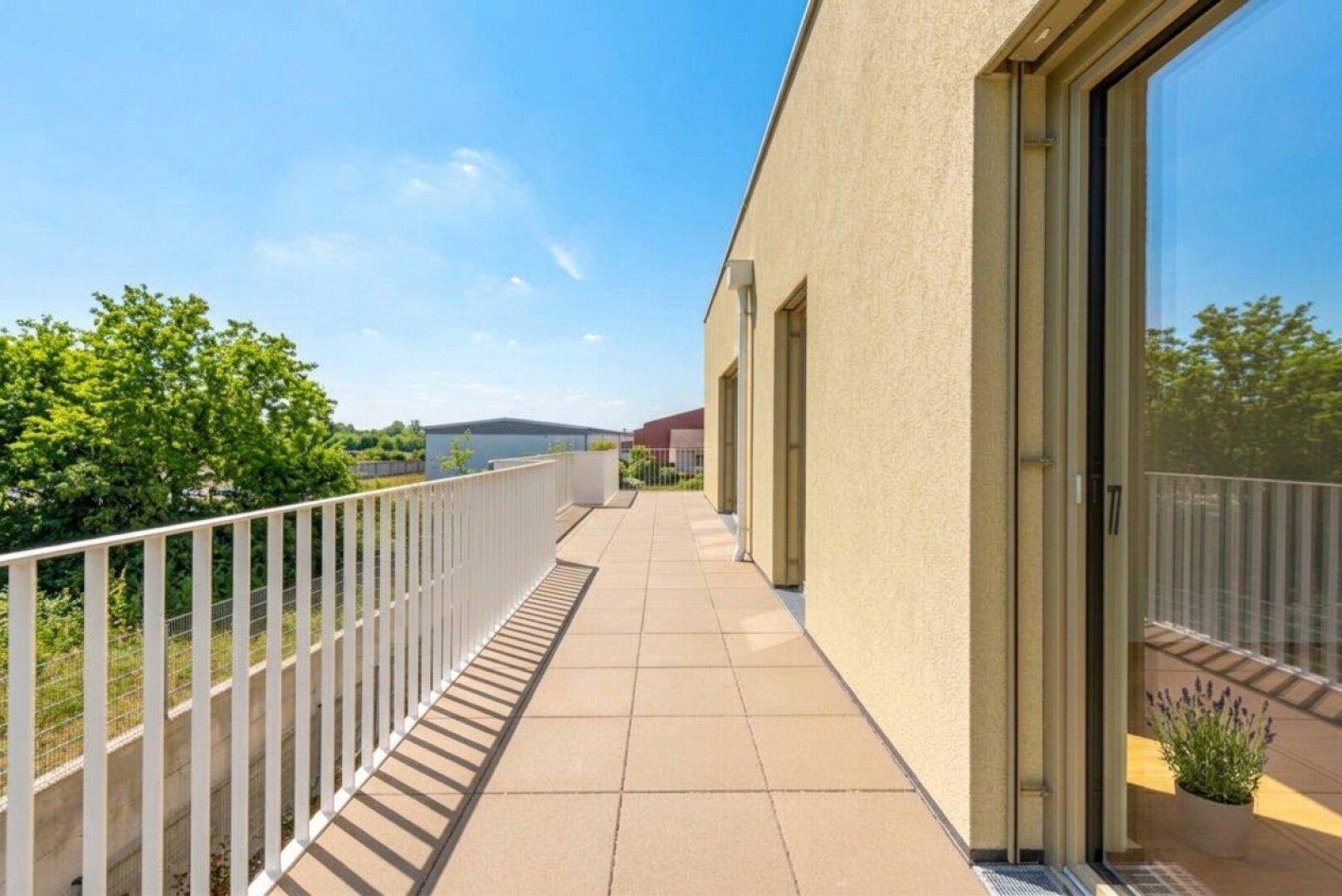 Lange, sonnige Terrasse mit Fliesenboden und Blick ins Grüne.