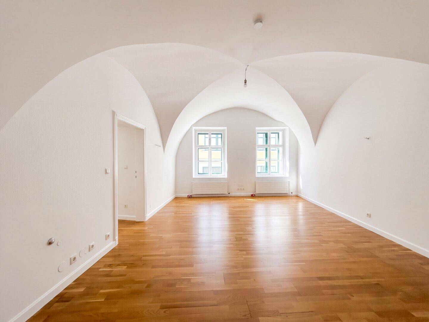 Heller, leerer Raum mit charakteristischer Gewölbedecke und warmem Holzboden, bietet vielseitige Nutzungsmöglichkeiten.